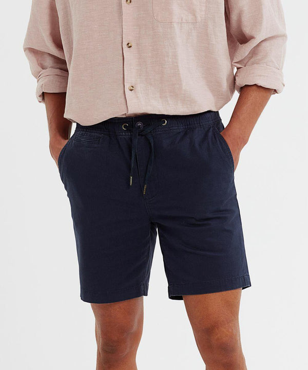 A person wearing a light pink long-sleeve Wombat WB902 button-up shirt with sleeves rolled up and navy blue drawstring shorts with hands in pockets.