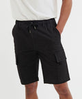 A person wearing a white Wombat WB903 shirt and black cargo shorts with hands in pockets stands against a plain background.