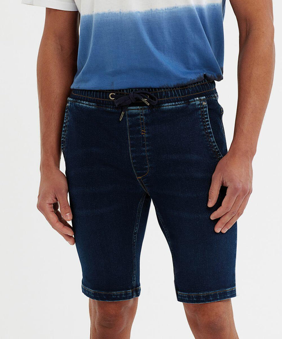 A person wears a blue and white shirt and dark denim Wombat WB907 shorts with a black drawstring. The shorts have pockets and visible stitching.