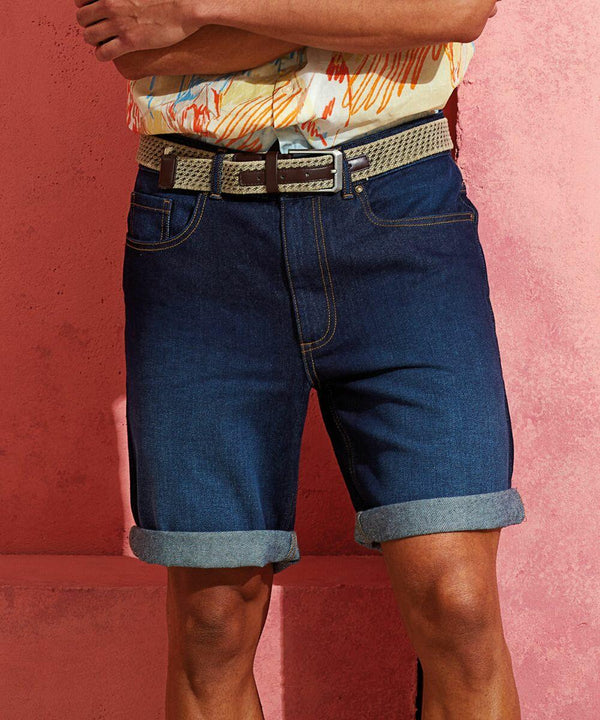 A person wearing a Wombat WB908 and rolled-up denim shorts stands in front of a pink wall with arms crossed.
