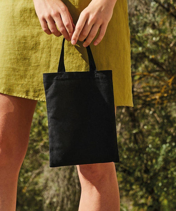 Person wearing a yellow dress holds a small black WM103 by Westford Mill by its handles outdoors, with greenery in the background.