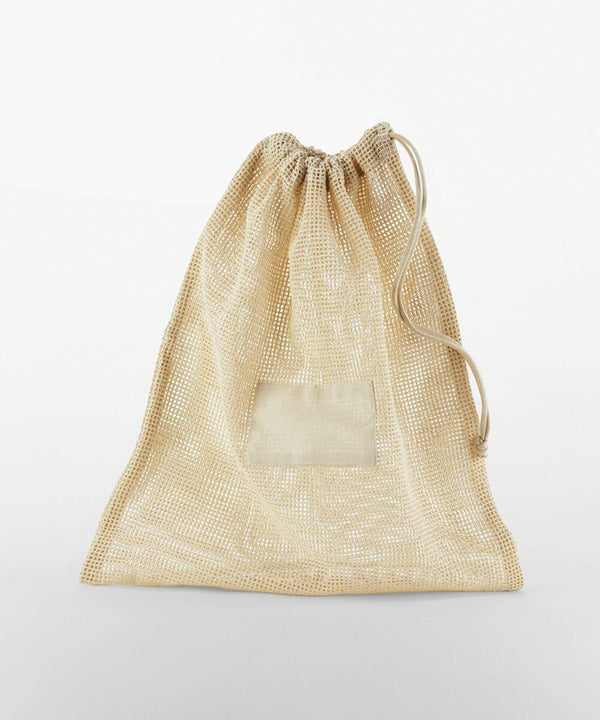 A beige mesh drawstring bag, WM155 by Westford Mill, with a small rectangular fabric patch on the front, placed against a plain white background.