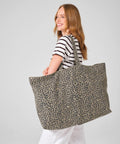 A woman with long light brown hair, dressed in a striped shirt and white trousers, carries the Westford Mill Leopard print canvas oversized tote bag over her shoulder against a plain light grey background.