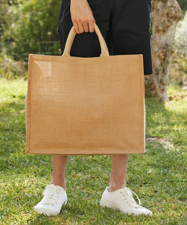 Person standing outside holding a large, rectangular, beige WM408 by its handles, wearing white shoes and black shorts. (Westford Mill)