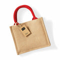 The WM412 by Westford Mill is a beige jute bag featuring strong red handles, displayed against a white background. A brown tag labeled 'jute' is affixed to one of the handles. The bag boasts a straightforward, eco-friendly design.