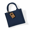 A Westford Mill WM412 jute tote bag in blue with round handles is displayed against a white background. Attached to one handle is a brown tag featuring the word "jute.