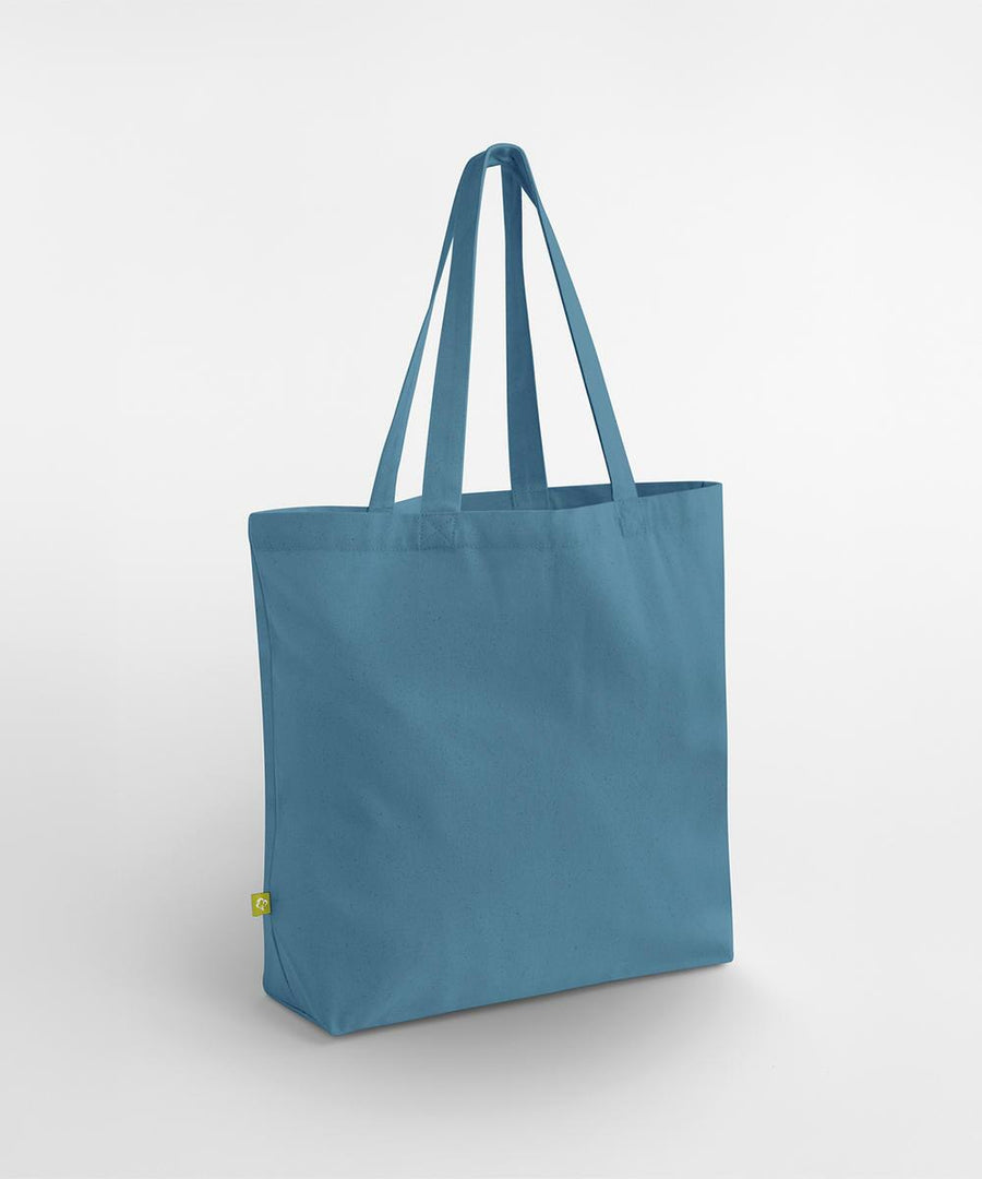 The Westford Mill EarthAware organic maxi bag for life, a plain blue canvas tote with two long handles and a small green side tag near the bottom seam, stands upright against a white background.