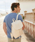 A man with a Westford Mill WM880 backpack walks down a sunlit street beside a building with a patterned wall.