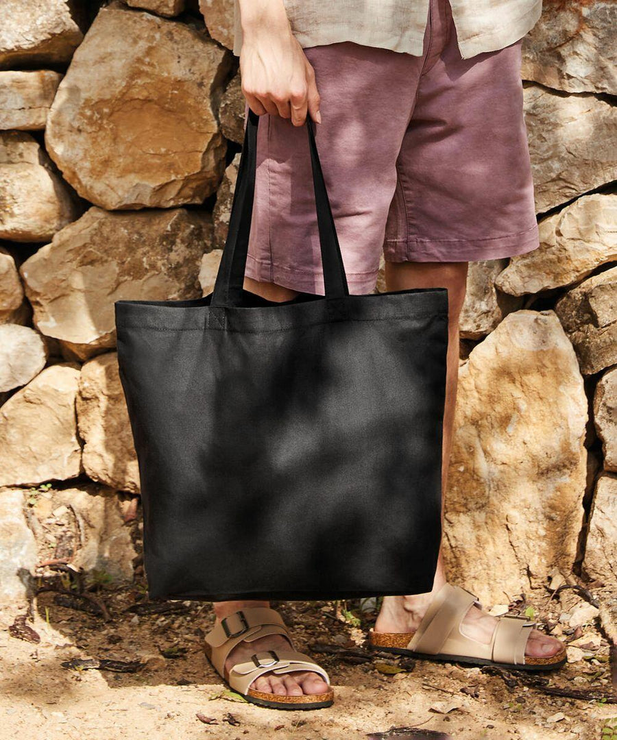A person wearing sandals and shorts holds a black Westford Mill WM925 in front of a stone wall.