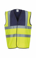 The Yoko YK001 is a high-visibility safety vest designed for visibility and safety in work environments. It features fluorescent yellow-green fabric with reflective silver-gray stripes and a solid navy blue panel across the shoulders.