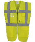 The Yoko YK002 is a high-visibility vest in bright yellow, featuring reflective gray stripes on the front and shoulders. It includes multiple pockets, a clear plastic ID holder, and a zipper closure.