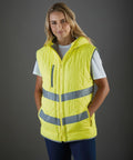 A person wearing a yellow Yoko YK026 quilted vest with reflective stripes over a white shirt stands against a gray background.