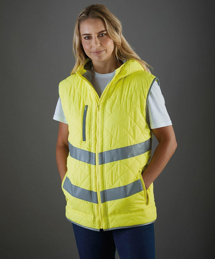 A person wearing a yellow Yoko YK026 quilted vest with reflective stripes over a white shirt stands against a gray background.