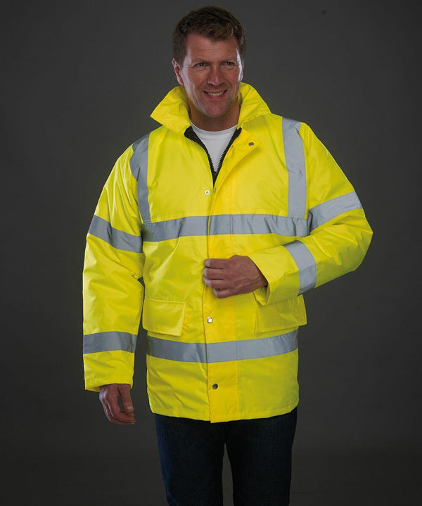 A man wearing a fluorescent yellow Yoko YK045 high-visibility jacket with reflective stripes stands against a plain dark background.
