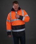 A person wearing a Yoko YK048 neon orange and navy blue high-visibility jacket with reflective stripes stands against a gray background.