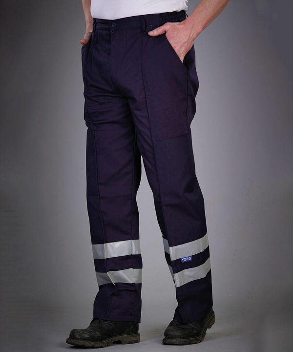 Person standing with hands in pockets, wearing Yoko YK074 navy blue work pants with reflective strips at the ankles.