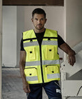 A person wearing a Yoko YK108 bright yellow safety vest stands indoors near a stair railing.