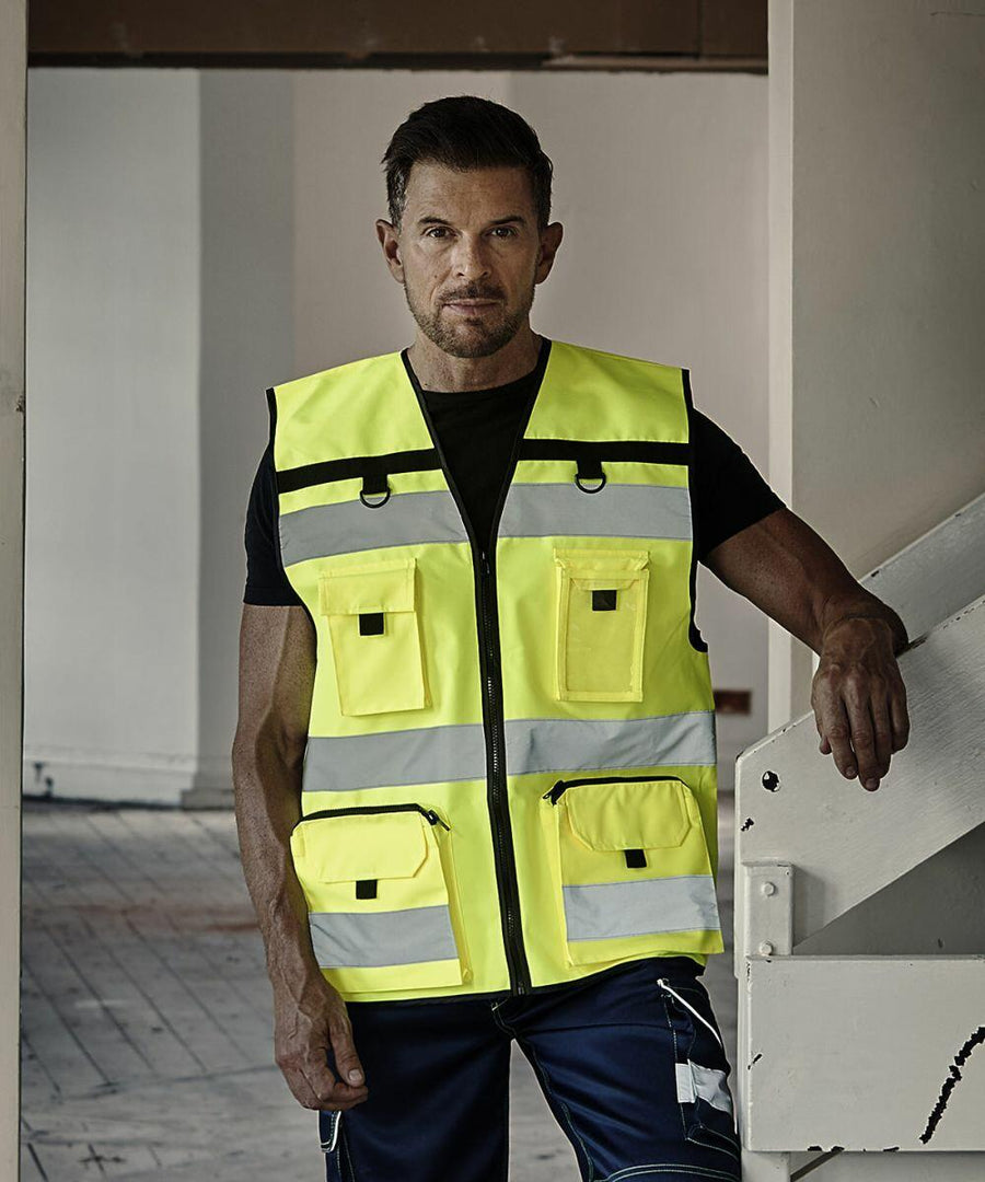 A person wearing a Yoko YK108 bright yellow safety vest stands indoors near a stair railing.