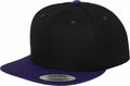 The cap, bearing the product name YP002 by Flexfit By Yupoong, features a black top with a purple brim and coordinating purple eyelets. A sticker on the brim reads "The Classic Snapback," highlighting its simple, two-tone design.