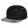 The Flexfit By Yupoong YP002 is a snapback hat featuring a primarily black design with a gray flat brim. The cap includes small gray ventilation holes and a gray button on top, along with a sticker on the brim.
