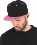 Man wearing a black and pink Flexfit By Yupoong YP002 looks down, dressed in a black shirt against a white background.
