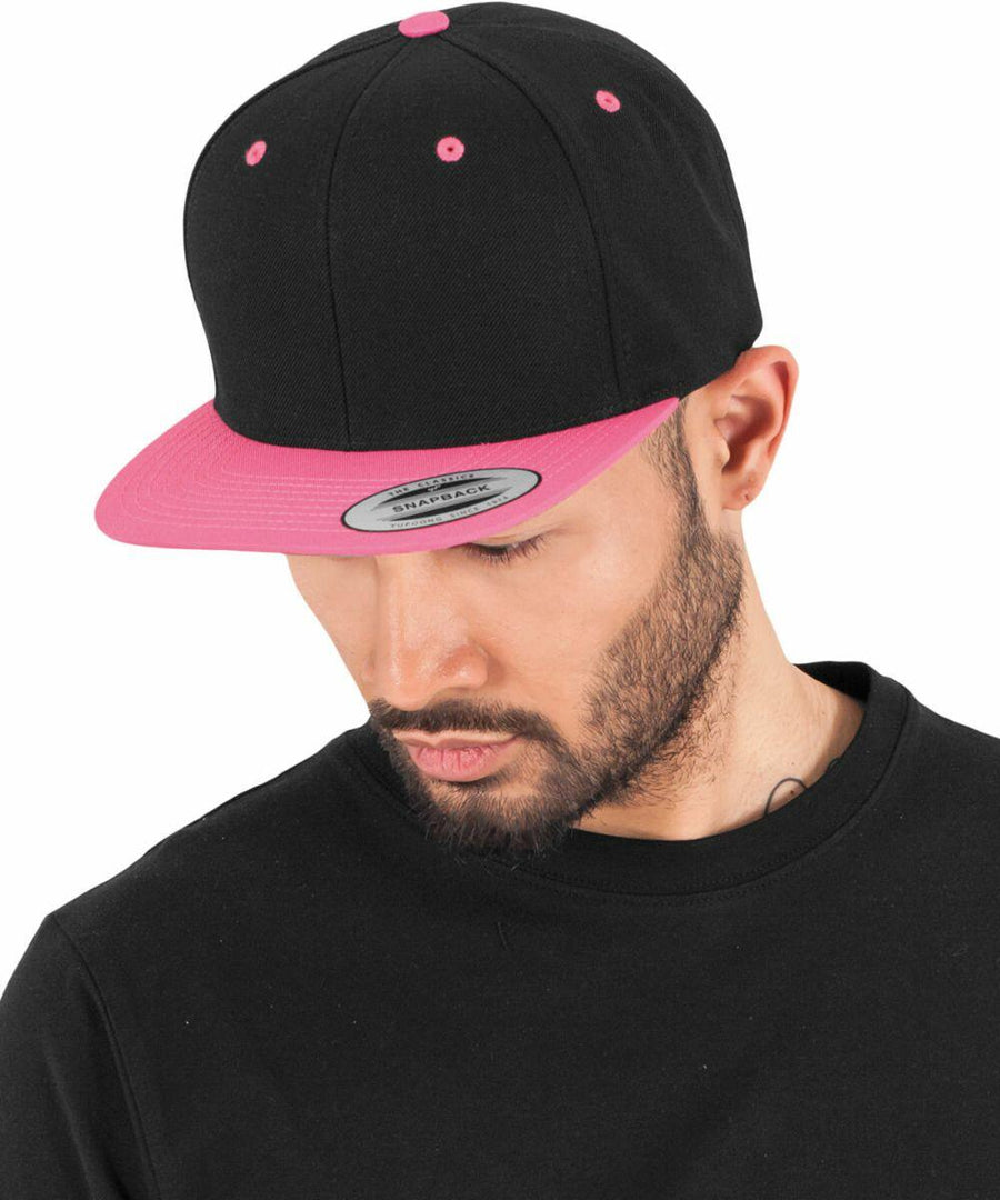 Man wearing a black and pink Flexfit By Yupoong YP002 looks down, dressed in a black shirt against a white background.