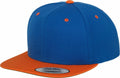 The YP002 by Flexfit By Yupoong is a blue snapback cap featuring an orange brim, an orange button on top, small orange eyelets, and a sticker on the brim.