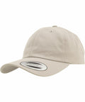 The Flexfit By Yupoong YP022 is a beige baseball cap featuring a curved brim and a circular sticker on the front. It includes ventilation holes on top and is displayed against a plain white background.