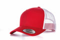 A Flexfit By Yupoong YP023 snapback trucker hat is displayed, featuring solid red front panels and a white mesh back. The curved brim of the hat highlights a circular sticker on the front, all positioned on a white surface.