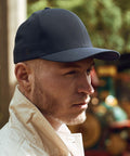 A person wearing a dark Flexfit By Yupoong YP028 baseball cap and a light jacket looks to the side outdoors.