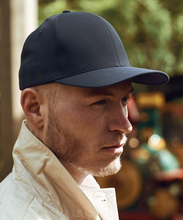A person wearing a dark Flexfit By Yupoong YP028 baseball cap and a light jacket looks to the side outdoors.
