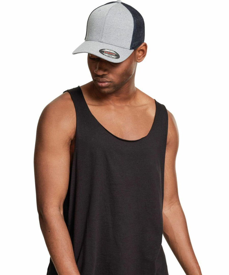 A man wearing a black sleeveless shirt and a gray and black Flexfit By Yupoong YP043 baseball cap looks downward with his left arm slightly extended away from his body.