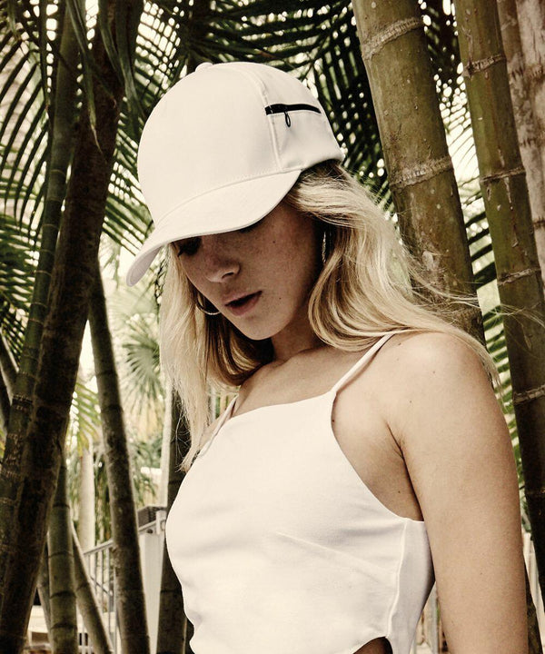 Person wearing a white cap (Flexfit By Yupoong YP065) and a white sleeveless top, standing in a forested area with bamboo in the background.