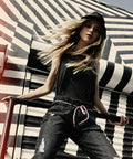 A person with long hair, wearing a black hat (Flexfit By Yupoong - YP069) and black outfit, poses against a backdrop with bold black and white stripes.