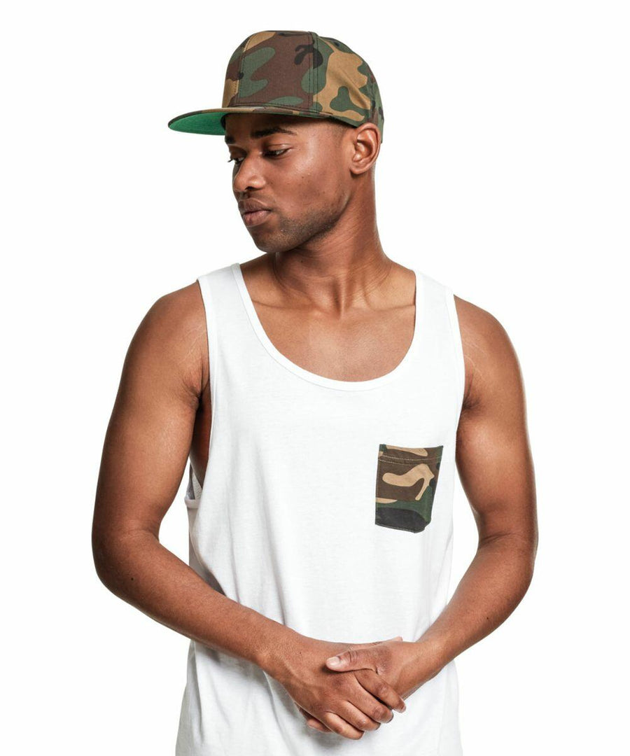 A man wearing a white tank top with a camo pocket and a Flexfit By Yupoong YP081 camouflage cap looks to his left against a white background.
