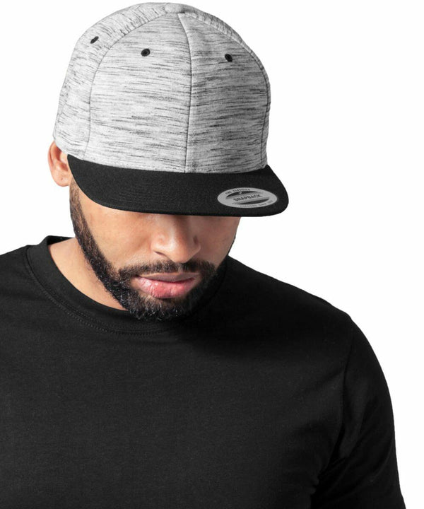 A man wearing a grey and black **Flexfit By Yupoong YP088** cap and a black T-shirt looks downward against a plain white background.