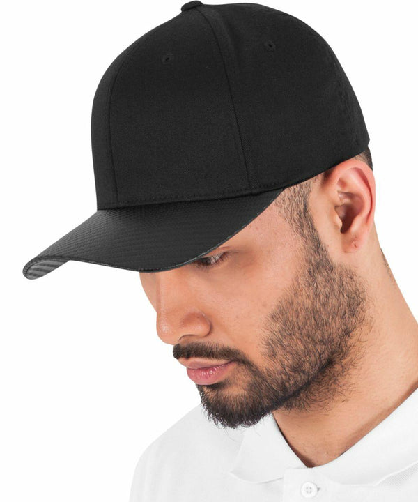 A person with facial hair wearing a Flexfit By Yupoong YP103 black baseball cap and white shirt, looking down.