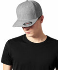 A person wearing a black t-shirt and a gray Flexfit By Yupoong YP117 with the brim facing forward, looking down.