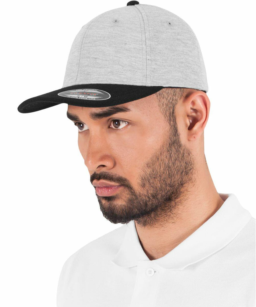 A man with a beard is wearing a light gray Flexfit By Yupoong YP133 cap with a black visor and a white polo shirt, facing slightly to the left.