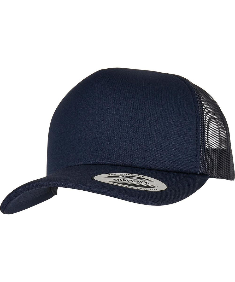 The YP Classics classic curved visor foam trucker cap (6320) by Flexfit by Yupoong is a navy blue hat with a curved peak, mesh back panels, snapback fastening, and a round "Snapback" sticker on the peak.