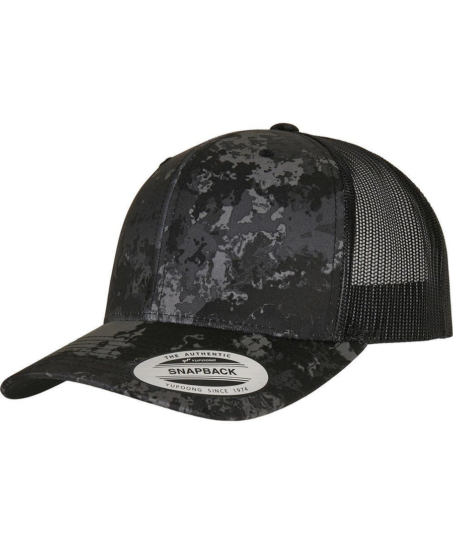 The Flexfit by Yupoong YP Classics Veil Camo retro trucker cap (6606VC) features a black and grey camo pattern, curved brim, black mesh back panels, and a round manufacturer sticker on the brim.