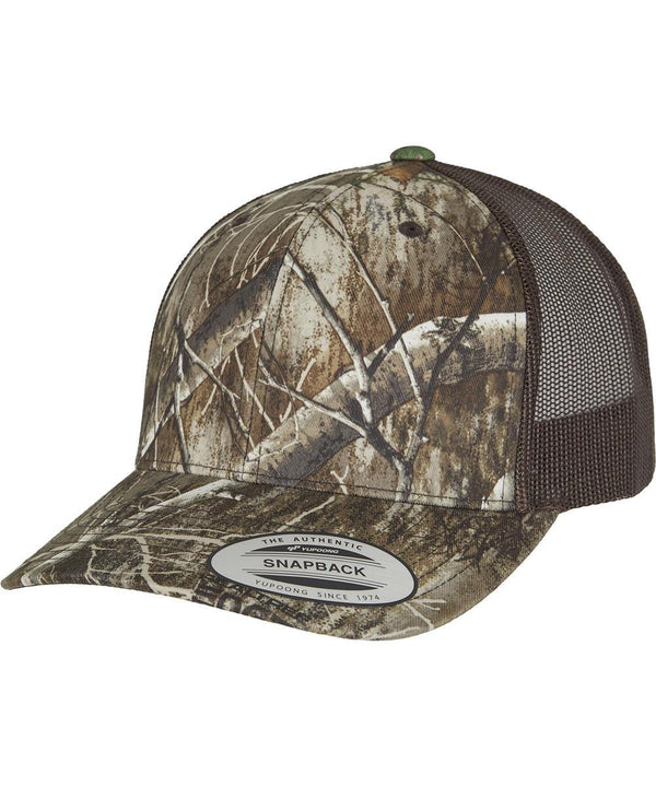 The YP Classics RealTree camo retro trucker cap (6606RC) by Flexfit by Yupoong features a camouflage front, brown mesh back, curved peak, and a "The Authentic Snapback Yupoong Since 1974" sticker on the peak.